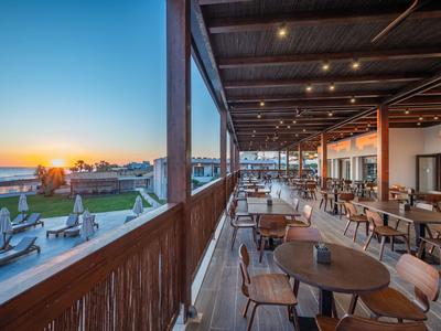 Offene Hotelterrasse mit Tischen und Stühlen, Meerblick bei Sonnenuntergang.