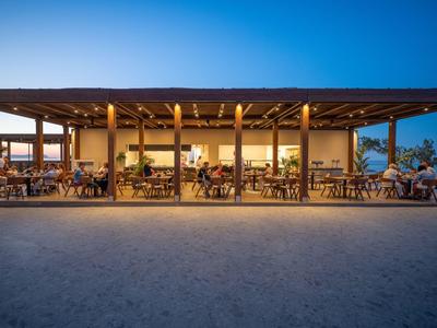 Offenes Restaurant mit Holzdach und Gästen bei Sonnenuntergang im Hotelumfeld.