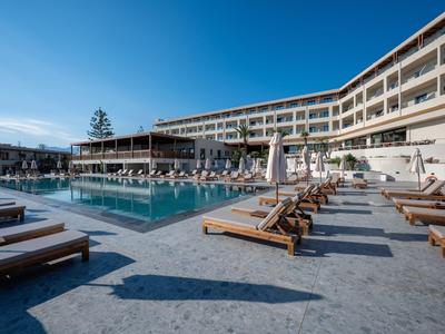Moderner Hotelkomplex mit großem Außenpool, Sonnenliegen und klarem blauem Himmel.