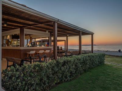 Offener Hotelbarbereich mit Sitzgelegenheiten bei Sonnenuntergang am Meer.