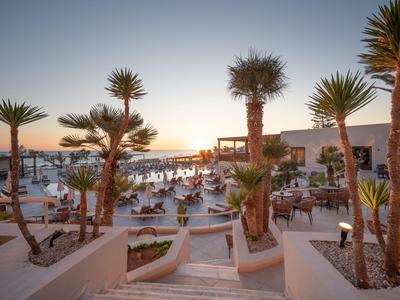 Sonnenterrasse mit Pool, Palmen und Sitzbereich bei Sonnenuntergang in einem Hotelresort.