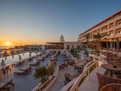 Luxuriöses Hotel mit Pool und Liegestühlen bei Sonnenuntergang am Meer.