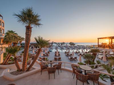 Terrasse eines Hotels mit Stühlen, Tischen, Palmen und Blick auf den Sonnenuntergang am Meer.