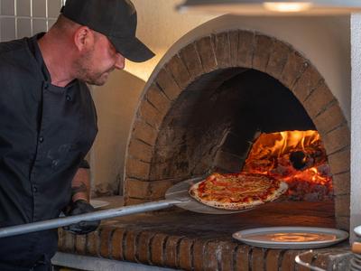 Ein Koch schiebt eine frisch gebackene Pizza aus einem traditionellen Steinofen.