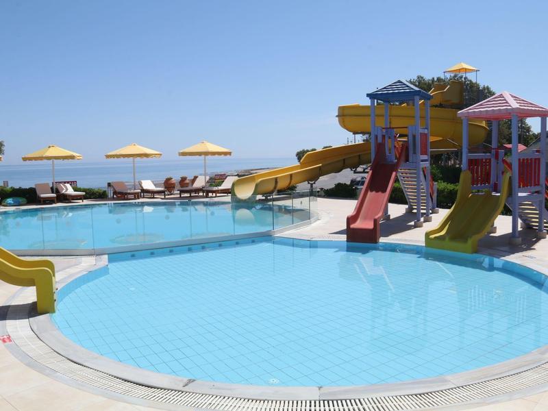 Children's play area with colorful slides and water slides next to a large pool with sun umbrellas.