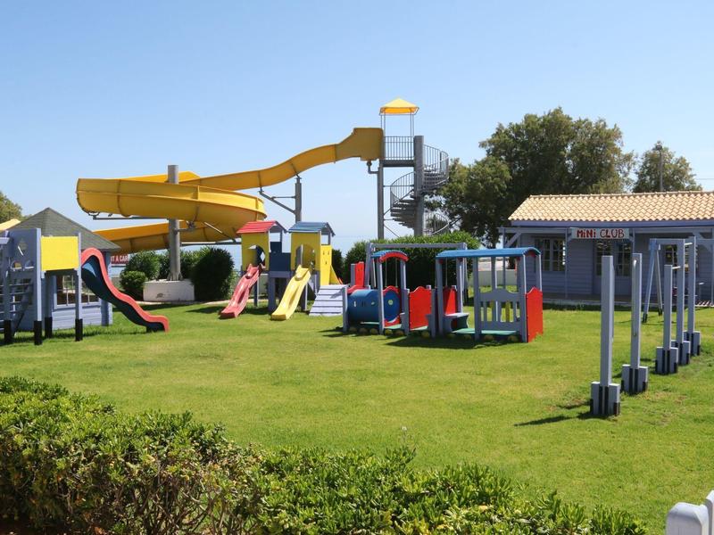 Playground with slides, climbing frames, and swings on green grass under a blue sky.