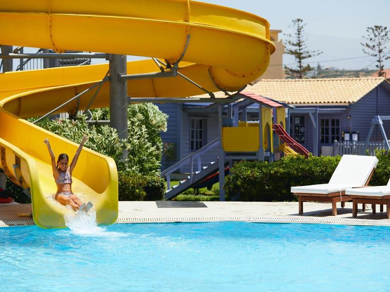 Woman slides down a yellow waterslide into a pool with lounge chairs in the background.