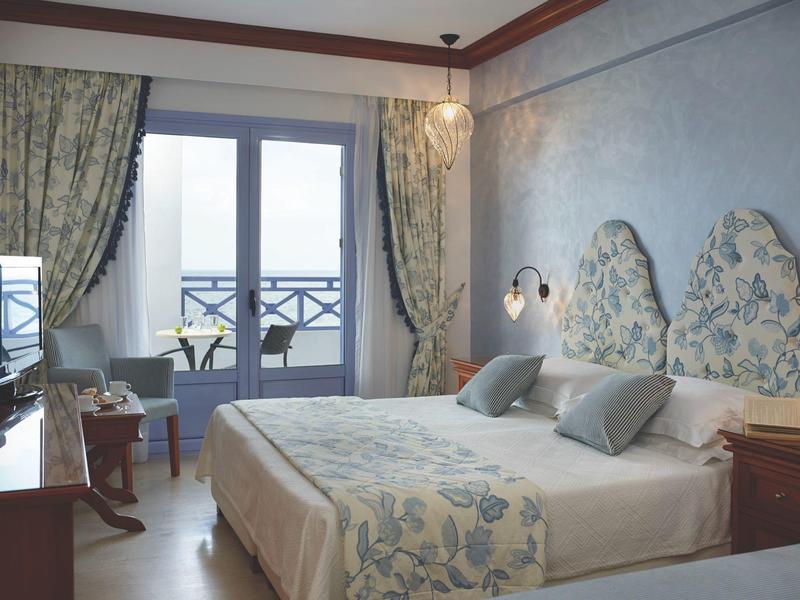A cozy hotel room with double bed, floral design, and balcony with view.