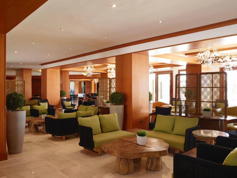 Cozy hotel lounge area with green armchairs, wooden tables, and warm wooden decor.