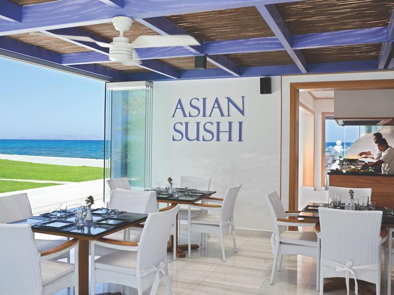 Modern sushi restaurant with sea view, white chairs, and open space.