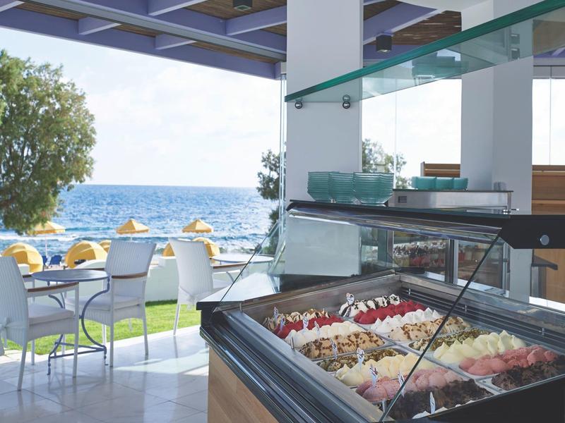 Ice cream shop with various flavors, tables and chairs with sea view in the background.