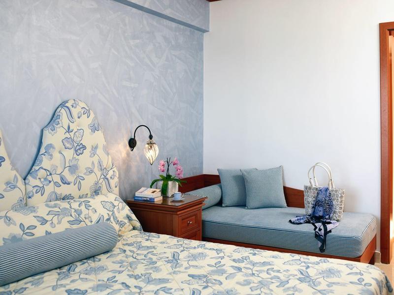 Brightly furnished hotel room with floral bedspread and cozy seating area with cushions.