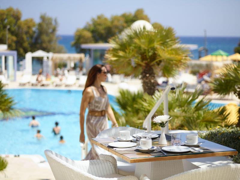 Table with tea set by the pool, woman nearby, sea visible in the background.