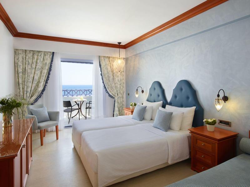 Bright hotel room with two beds and balcony overlooking the sea.