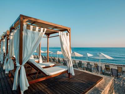 Großes Strandbett mit weißen Vorhängen auf Holzdeck am Sandstrand mit Meeresblick.