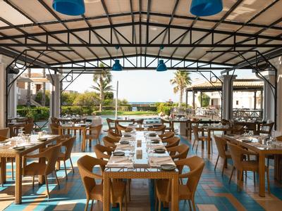 Open hotelrestaurant met houten tafels, stoelen en uitzicht op tuin en zee.