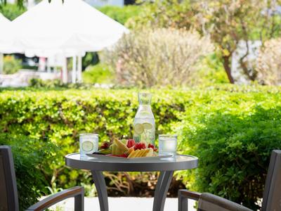 Een buitenterras met een tafel met een fles water, glazen en een kom fruit bij zonnig weer.