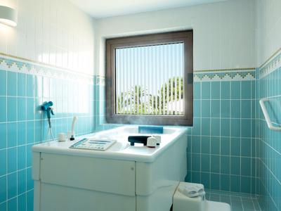 Lichte badkamer met turquoise tegels, groot bad en raam met uitzicht op groen.