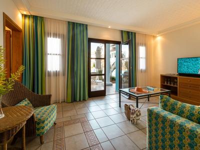 Lichte woonkamer met groene gordijnen, comfortabele fauteuils en uitzicht op het hotelterras.