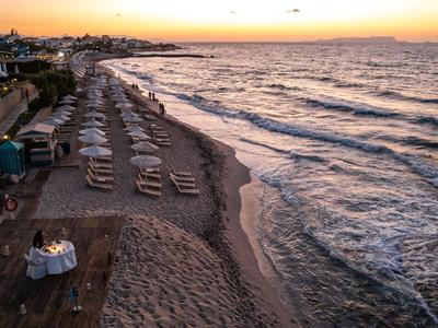 Een strand met ligstoelen en parasols bij zonsondergang naast rustige golven.