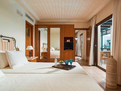 Hotelový pokoj s manželskou postelí, dřevěnou skříní a balkonem s venkovním posezením.