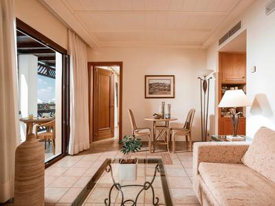 Světý obývací pokoj s béžovou pohovkou, skleněným konferenčním stolkem, jídelním koutem a velkými okny s výhledem na balkon.