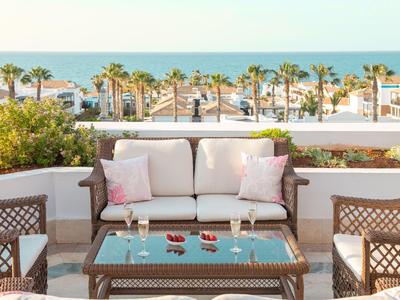 Terrasse mit Rattanmöbeln, Blick auf Palmen und das Meer im Hintergrund bei sonnigem Wetter