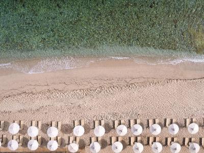 Letecký pohled na pláž s rovnoměrně uspořádanými slunečníky a lehátky podél pobřeží.