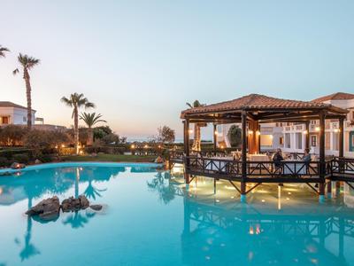 Großer Pool mit klarem Wasser, umgeben von Pavillons und Palmen bei Sonnenuntergang.