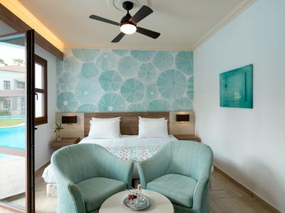 Moderní hotelový pokoj s manželskou postelí, tyrkysovými křesly a přístupem k bazénu.