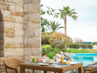 Terrasse mit Holztisch und Stühlen neben einem Pool in einer mediterranen Hotelanlage.