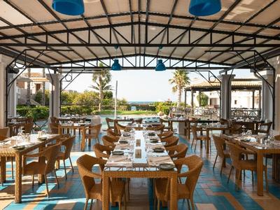 Offener Restaurantbereich mit eingedeckten Tischen und Blick auf Garten und Meer.