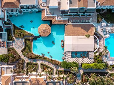 Luchtfoto van een hotelzwembad met parasols, omgeven door gastenkamers en groen.