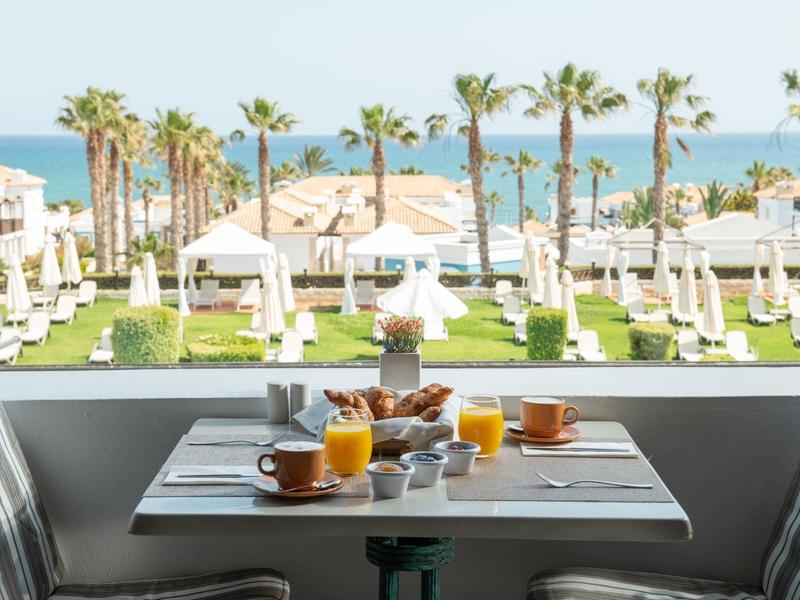 Stůl na snídani na balkóně s výhledem na bazén, palmy a moře v tropickém hotelu.