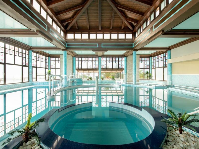 Vnitřní bazén s vířivkou, velkými okny a dřevěnými stropy v hotelu.