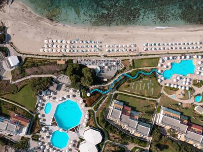 Luftaufnahme eines Resorts mit mehreren Pools, Liegestühlen am Strand und klarem türkisfarbenem Wasser.