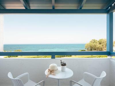 Balkon mit weißem Tisch, zwei Stühlen, Blick aufs Meer und blauen Balken-Geländer.