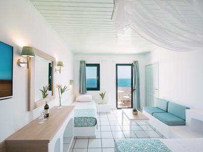 Helles, modernes Zimmer mit weißen Wänden, Bett, Sofa, Fernseher und Blick auf Meer durch Fenster.