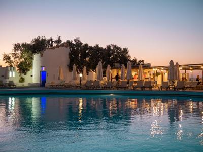 Beleuchtetes Hotel mit Pool und Sonnenschirmen bei Sonnenuntergang.