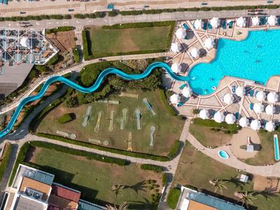 Luftaufnahme eines Resorts mit Pool, Liegestühlen und einem langen blauen Wasserweg.