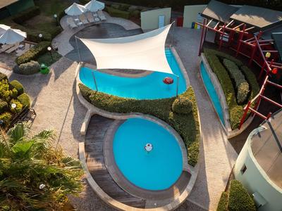 Blick auf einen Hotelpool mit markantem Sonnensegel und Rundpool im Tageslicht.