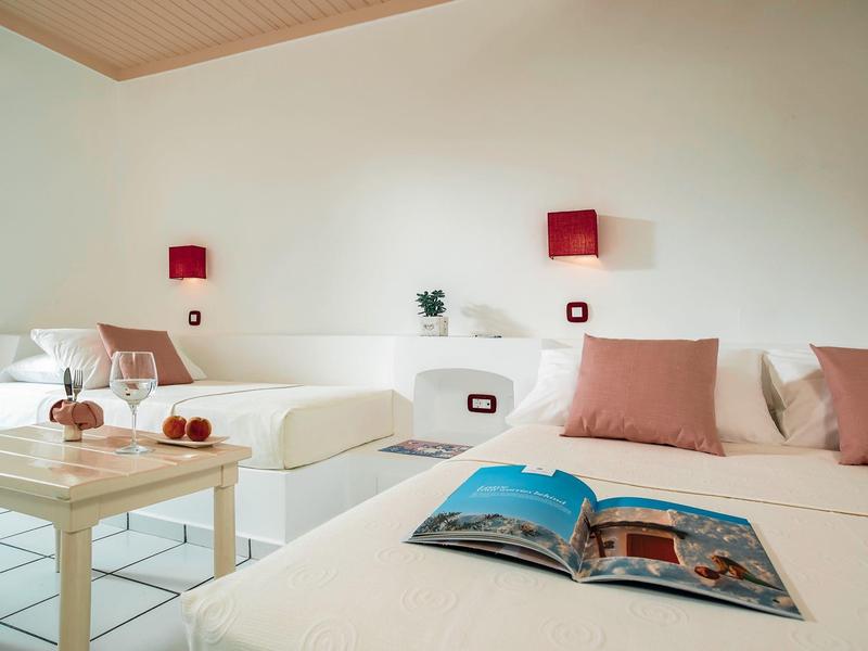 Helles Schlafzimmer mit zwei Betten, roten Wandlampen, Kissen und offenem Buch auf dem Bett.