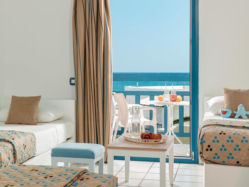Modernes Wohnzimmer mit Sofa, Polsterhocker und offener Balkontür zum Meer und weißem Balkon.