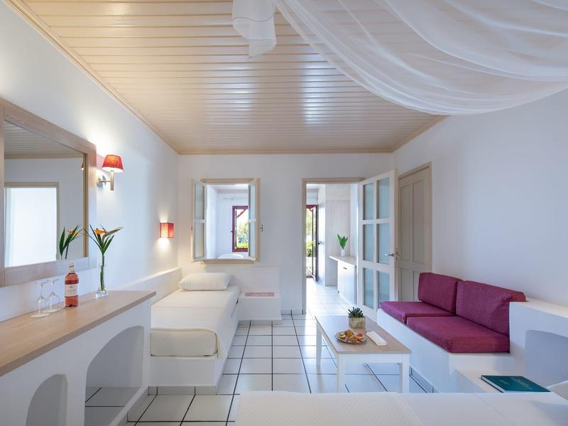 Helle Wohnküche mit weißen Fliesen, roten Sofa, Esstisch und großen Fenstern.