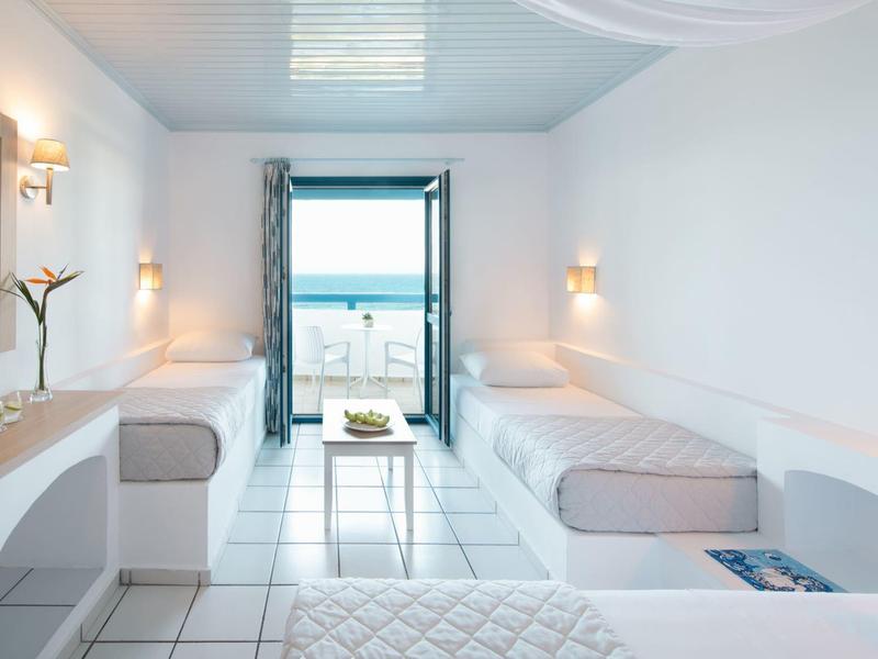 Helles, schlichtes Zimmer mit zwei Einzelbetten, kleinem Tisch und offenem Fenster zum Meer.