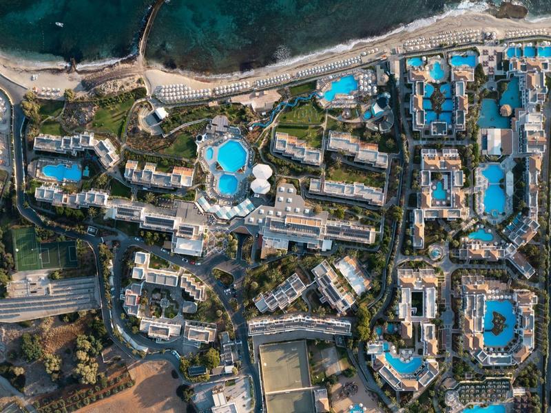 Luftaufnahme einer Küstenstadt mit zahlreichen blauen Pools und Gebäuden in hellem Beige.