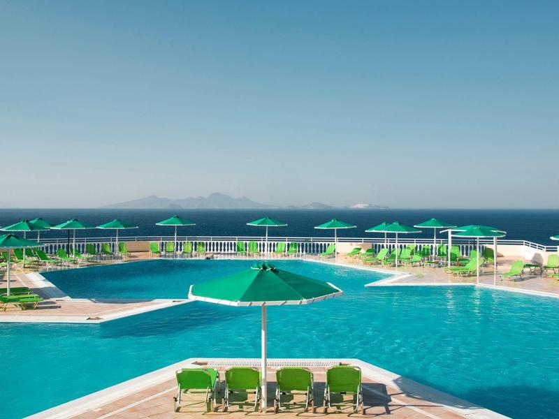 Großer Außenpool mit grünen Sonnenschirmen und Liegestühlen mit Blick aufs Meer.