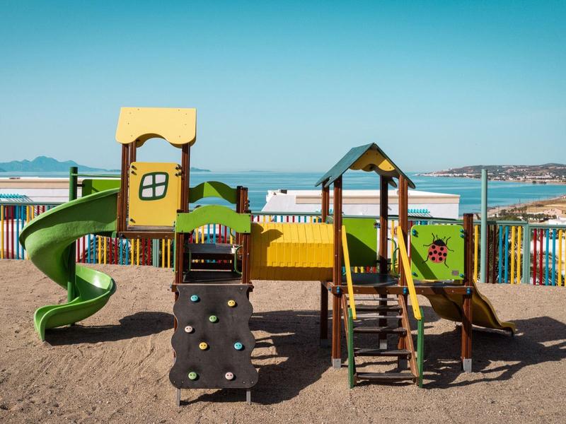 Bunter Kinderspielplatz mit Rutsche und Kletterelementen am Strand mit Meerblick.