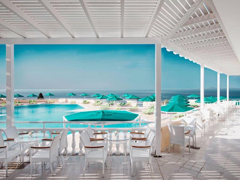 Moderner Poolbereich mit weißen Stühlen und blau-grünen Sonnenschirmen am Meer