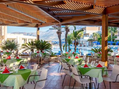 Offenes Restaurant mit grün karierten Tischtüchern, roten Servietten und Blick auf Pool und Palmen.